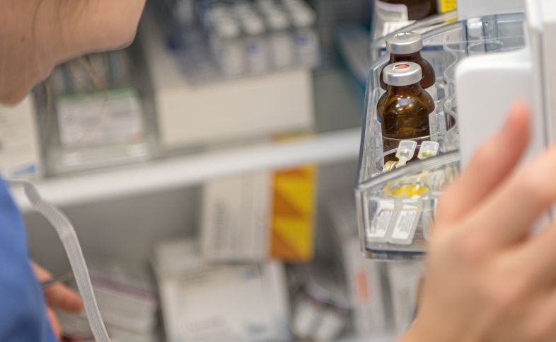 Pharmacy fridge held open by person in scrubs. Medications can be seen in door of fridge.