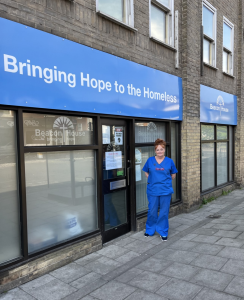 Michelle, advanced nurse practitioner, stands outside Beacon House Ministries in blue scrubs. 