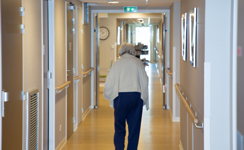 Elderly lady walks away from the camera down a corridor