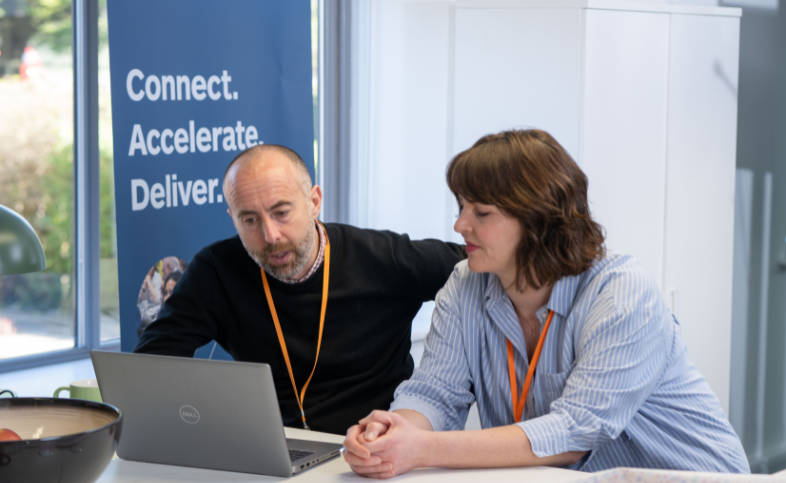 Ben and Deb look at a laptop together - connect, accelerate and deliver written in the background
