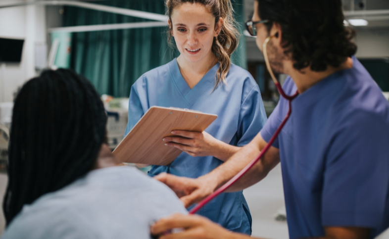 Two medical professionals in blue scrubs talk to patient