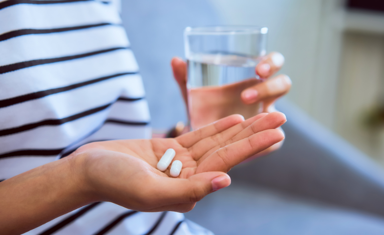 Person holds tablets in the palm of one hand while holding a glass of water in the other