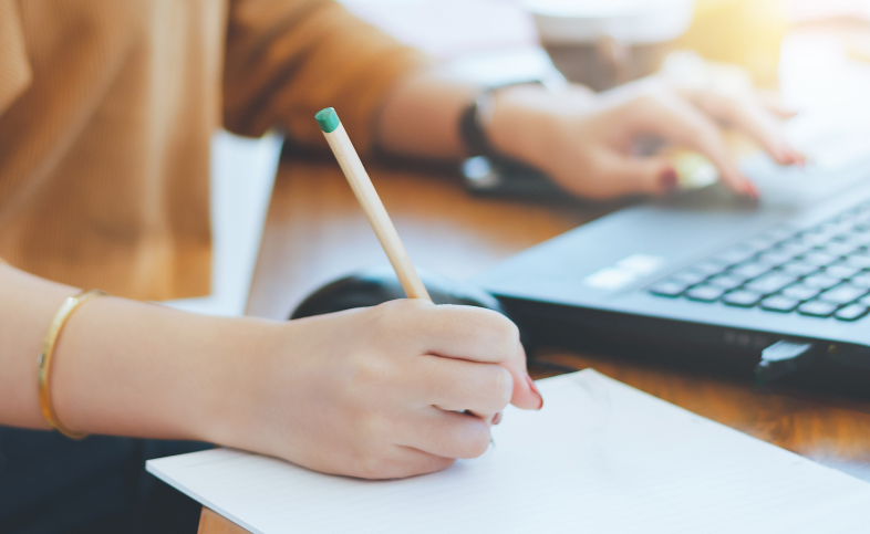 Someone holding a pencil to write while looking at a laptop