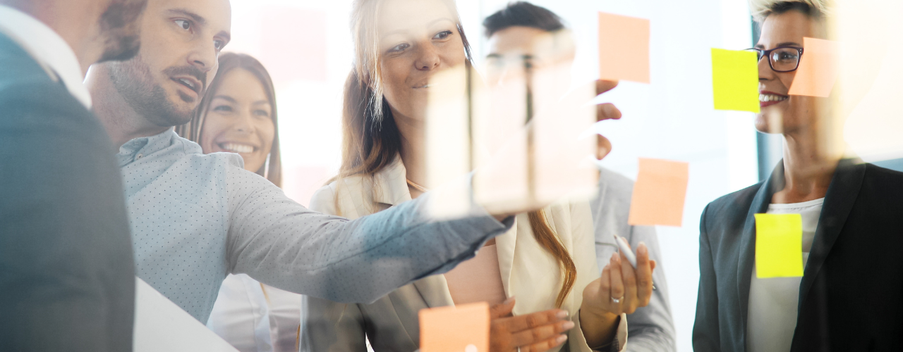 People work together, placing post-it notes on a glass screen