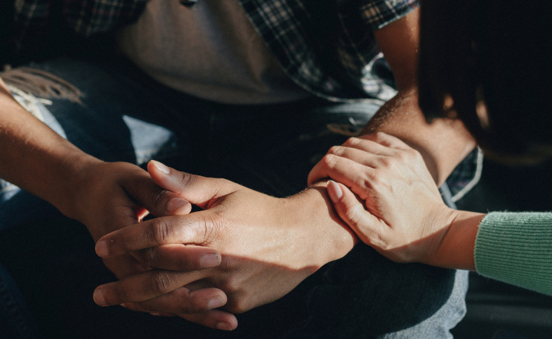 Hand is placed on the arm of an individual in a supportive, caring fashion.