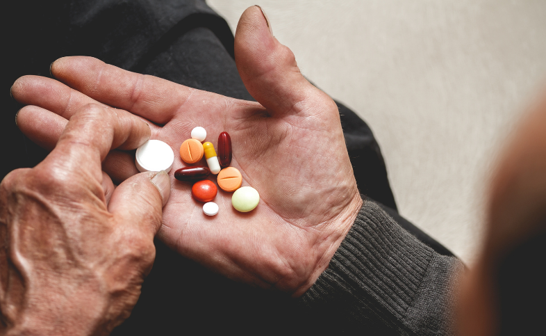 Hand of elderly person with a selection of different coloured and shaped tablets in the centre
