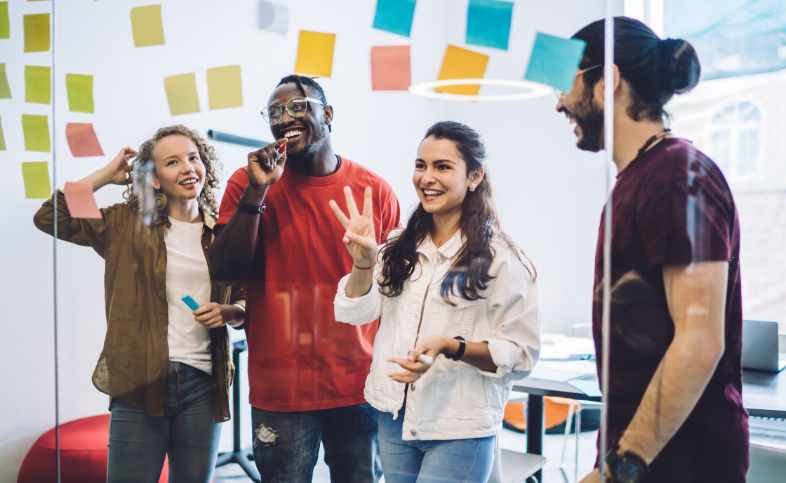 Four colleagues stand on one side of a screen of glass together looking at multicoloured postit notes