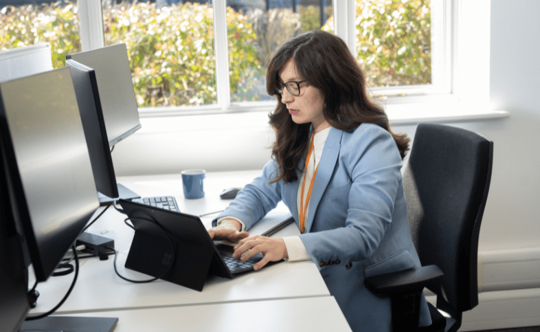 Women in a light blue blazer types on her computer