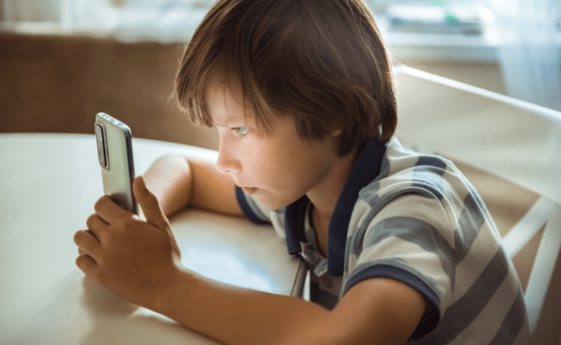 Child in stripey blue and white top looks closely at a mobile phone in his hands