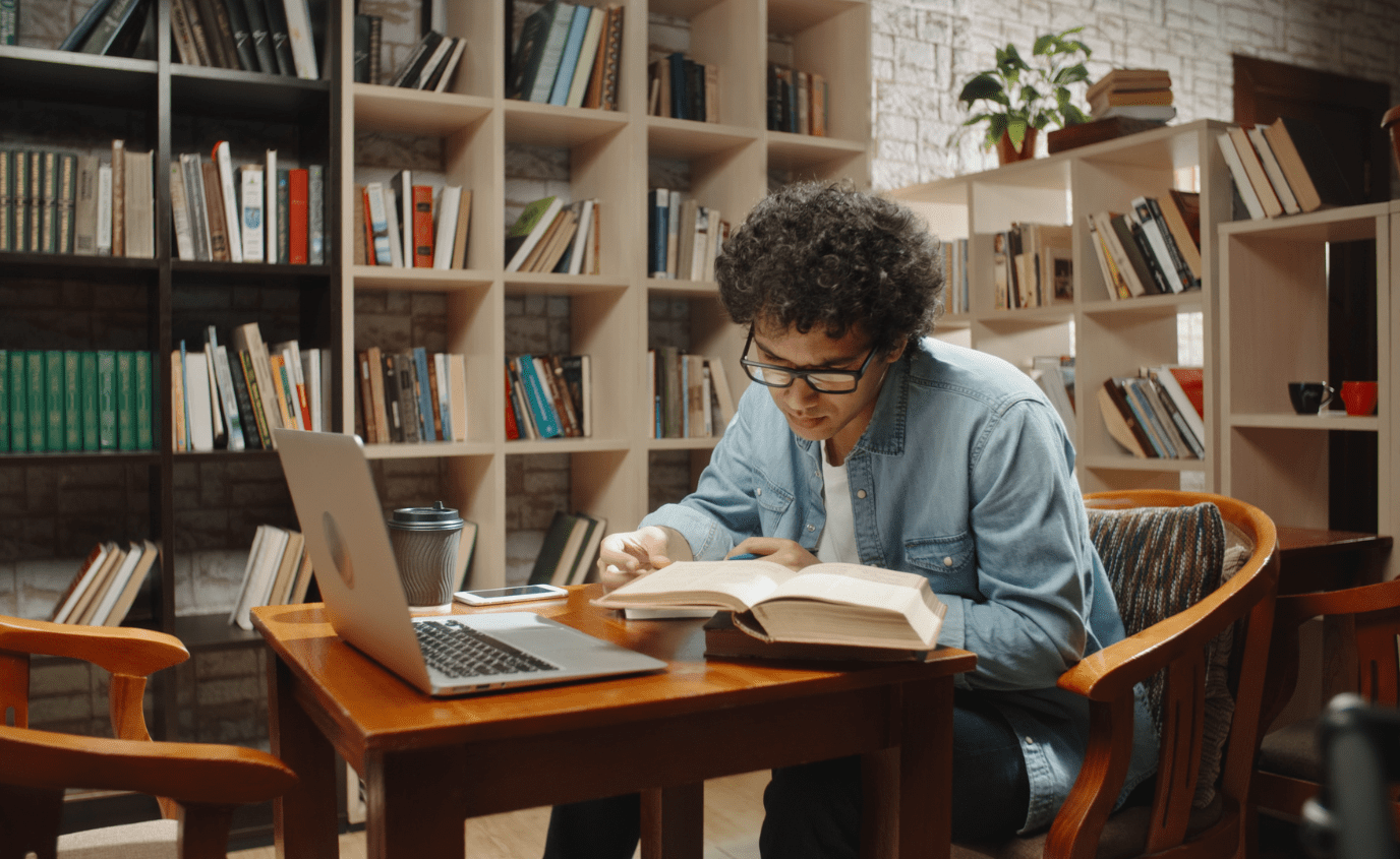 Curly haired man in library, looks at book