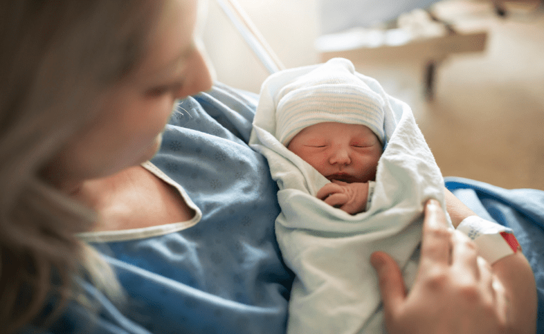 Newborn baby held in mother's arms as they sit in a hospital bed