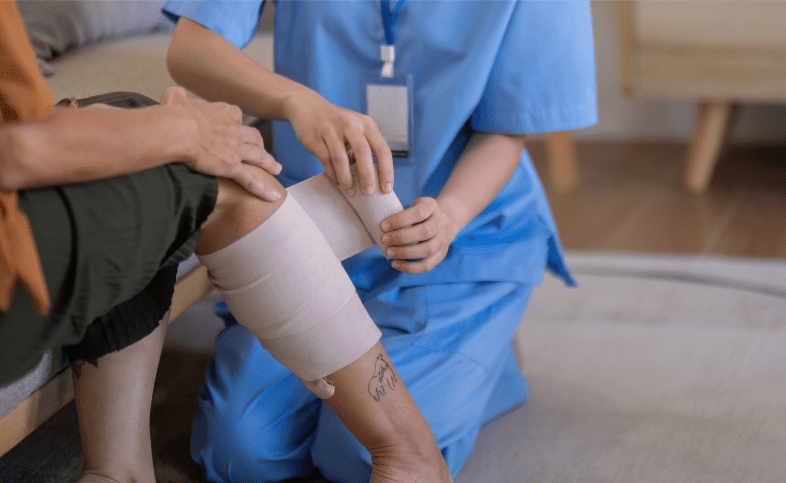 Person in scrubs wrapping a bandage around someone's leg